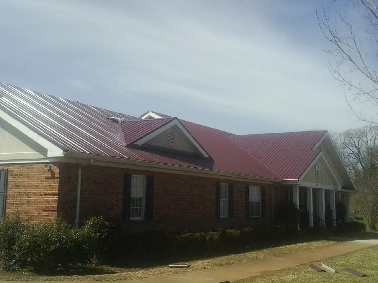 Red metal roof with gabled entries on a long brick building, from a Hail Damage Roof Repair job in Berkeley